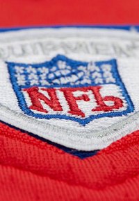 Embroidered NFL shield logo with a blue crown and red letters on a white patch over red fabric.