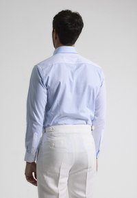 Camisa a rayas azul claro con un cuello firme, combinada con pantalones blancos que cuentan con un bolsillo trasero y tabuladores laterales ajustables.