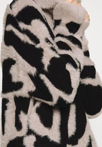 Cappotto in pelliccia artificiale con un motivo astratto in nero e beige, caratterizzato da una texture morbida, vestibilità comoda e maniche lunghe.