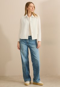 Vit texturerad väst med krage, knappstängning, bärs över en långärmad vit skjorta och ljusblå vida jeans med en avslappnad passform.