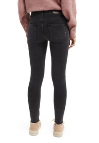 Jeans skinny negros con una textura suave, que cuentan con dos bolsillos traseros y un sutil efecto de desgaste, combinados con deportivas de color claro.