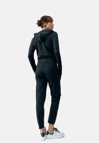 Felpa sportiva nera con un design aderente, maniche lunghe e cappuccio. Abbinata a pantaloni neri a gamba affusolata e sneaker bianche.