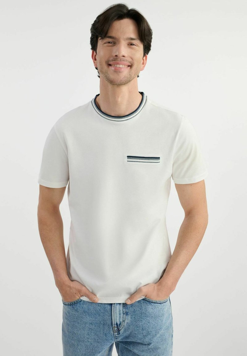 Biała koszulka z krótkim rękawem i okrągłym dekoltem, z granatowym paskiem na kołnierzyku oraz kieszenią z pasującym paskiem.