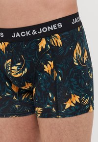 Schwarze Boxershorts mit einem tropischen Blattmuster in Grün und Gelb, ausgestattet mit einem elastischen Bund, der mit "JACK & JONES" beschriftet ist. Weiches, dehnbares Material.
