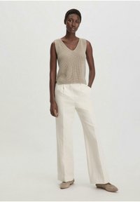 Canotta beige in maglia con scollo a V, abbinata a pantaloni bianchi a gamba larga. Il modello si trova su uno sfondo neutro, mettendo in risalto trame e colori morbidi.