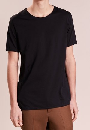 Czarny t-shirt z krótkim rękawem, wykonany z miękkiej tkaniny, z okrągłym dekoltem i luźnym krojem, w połączeniu z brązowymi spodniami. Gładki wzór, bez nadruków.