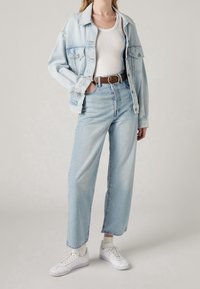 Chaqueta de mezclilla azul claro con un corte relajado, combinada con unos jeans azul claro de talle alto. Una camiseta sin mangas blanca, cinturón marrón y zapatillas blancas completan el look.