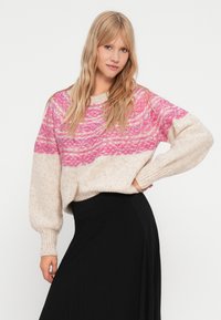 Maglione lavorato a maglia con un motivo ondulato rosa e crema, vestibilità ampia, maniche larghe, texture morbida, abbinato a una gonna nera.