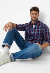 Karierte Hemd in Blau und Rot, Knopfverschluss, aus Baumwolle, kombiniert mit hochgekrempelten blauen Jeans und weißen Sneakers.