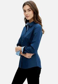 Navy blue button-up shirt with long sleeves; features a contrasting light blue collar and cuffs; made from a smooth fabric.