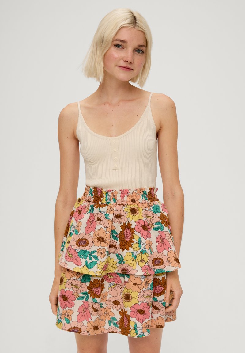 Débardeur crème à côtes avec des boutons, associé à une jupe florale multicolore à deux couches et une taille élastique.