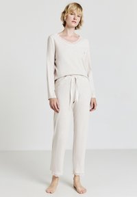 Completo da loungewear beige chiaro con maniche lunghe, scollatura a V e bordo in pizzo; pantaloni con coulisse e gambe affusolate, tessuto morbido e vestibilità rilassata.