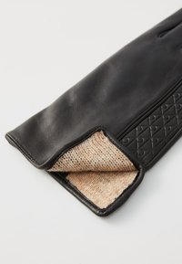 Svart lærhanske med et teksturert, kviltet mønster på utsiden og en myk beige fleecefôr. Mansjetten er pent ferdig.