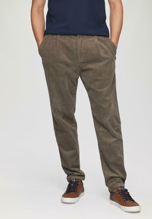 Bruine corduroy broek met verticale strepen, uitgerust met een relaxte pasvorm, zijzakken en gestyled met bruine en marineblauwe sneakers.