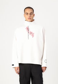 White zip-up sweatshirt featuring pink floral design and "CARRIEDLUCCI" text. Long sleeves with a black detail at the cuffs.