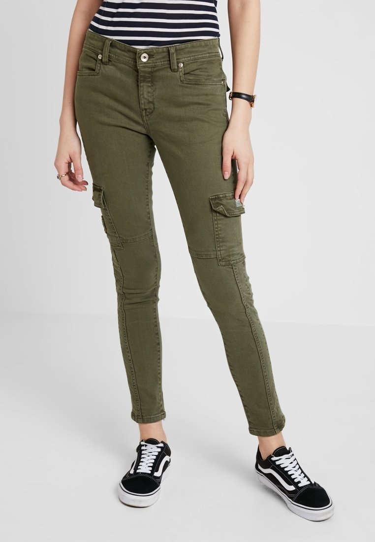 Pantalones cargo verde oliva de corte ajustado, con bolsillos delanteros y costuras en las rodillas; combinados con zapatillas negras y una camisa a rayas.
