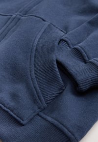 Sweatshirt bleu marine présentant une texture douce, des poignets et un ourlet côtelés, ainsi qu'une poche avant avec un motif cousu.