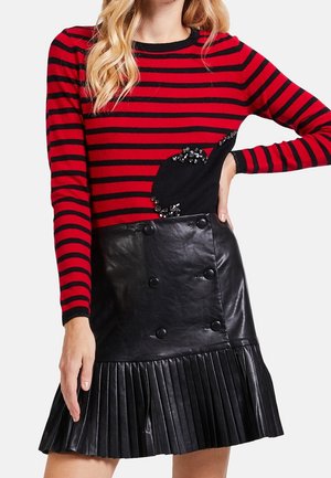 Punainen ja musta raidallinen neule, jossa on paljettitietoa; yhdistetty mustan pleatattu nahkahameeseen, jossa on kaksiriviset napit.