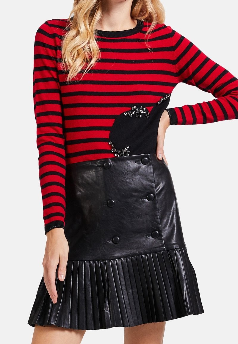 Rot und schwarz gestreifter Pullover mit Paillettendetails; kombiniert mit einem schwarzen, gefalteten Lederrock mit doppelt geknöpften Knöpfen.