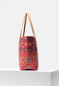 Bolso tote de patrón rojo con una forma estructurada, asas de cuero beige y diseños florales intrincados en azul y amarillo. Textura suave.