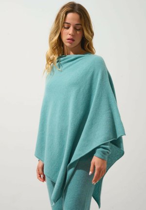 Un poncho tricoté de couleur bleu clair avec un design drapé, une texture douce et des manches longues, complété par un pantalon ajusté assorti.