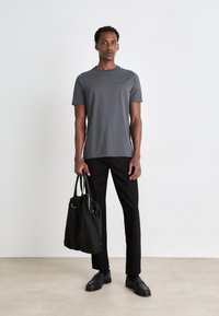Grå T-shirt med korte ærmer, sorte bukser og sort taske med metaldetaljer. Glat stoftekstur, minimalistisk design.