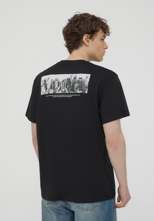T-shirt in cotone nero con una grafica orizzontale in bianco e nero di un paesaggio urbano sul retro, colletto tondo e maniche corte.