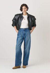 Juodas odinis bombonešis su pūstu rankovėm, baltas prilipęs marškinėliai, aukštos juosmens mėlyni džinsai ir rudi auliniai batai iki kulkšnies.