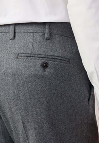Donkergrijze broek van gestructureerde stof, met een knoopzak aan de achterkant en riemlussen. De tailleband is gecombineerd met een wit shirt.