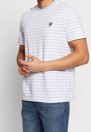 Hombre vistiendo una camiseta de rayas horizontales azul claro y blanca con un pequeño logo de un pájaro amarillo en el pecho, combinada con jeans azules.