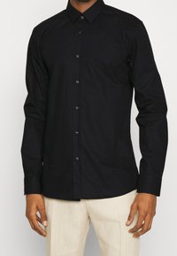 Camisa negra de manga larga abotonada con cuello, hecha de una tela suave. Presenta un ajuste entallado, con botones negros a juego en la parte delantera.