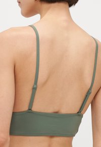 Zelený bezšvový bralette s nastaviteľnými ramienkami, hladkou textúrou a zjednodušeným dizajnom. Obsahuje široký pás a minimálne švy.