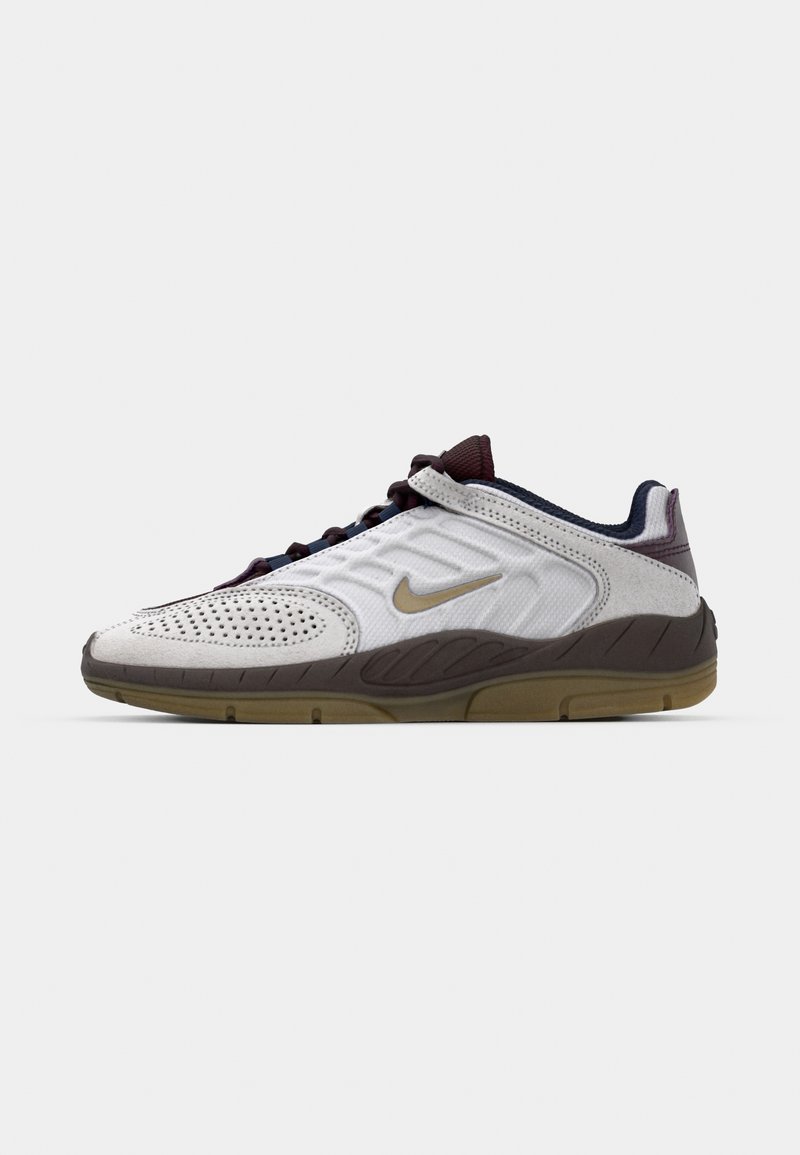 Chaussure de sport blanche avec un dessus perforé, des accents violet foncé et une semelle en caoutchouc. Elle présente un logo Nike en or sur le côté.