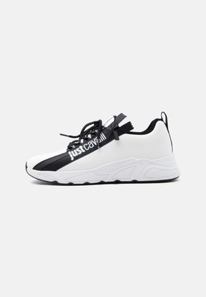 Hvit og svart joggesko med tykk såle, svarte lisser, sideglidelås og "just cavalli"-merke på den svarte stripen over overdelen.