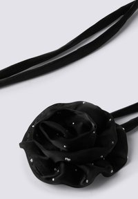 Accessorio per capelli in tessuto nero a forma di rosa, decorato con piccoli accenti lucidi, dotato di due nastri in tessuto nero per la chiusura.
