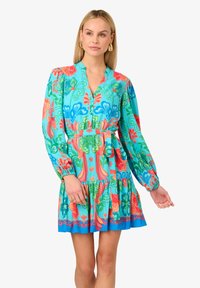 Abito stampato floreale multicolore con scollo a V, maniche lunghe a sbuffo, cintura da legare in vita e orlo a strati con volant. Il materiale sembra leggero.
