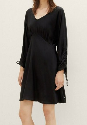 Robe noire avec un décolleté en V, des manches longues avec des détails froncés, et une taille cintrée. Tissu lisse et léger avec un ourlet légèrement évasé.