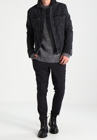 Svart denimjacka med två framfickor, grå stickad tröja under, och åtsittande svarta byxor. Svarta snörade ankelskor.