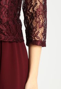 Bordeaux klänning med spetsöverdel och blommönster, trekvartsärmar och en slät kjol i tyg. Texturerad och lagerdesign.