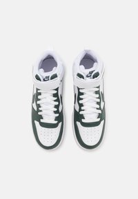 Ett par vita och mörkgröna Nike högskor med snörning och kardborreband, fotograferade ovanifrån på vit bakgrund.