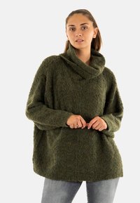 Groene textuur cowl-neck trui met een losse fit, lange mouwen en een zachte afwerking. Gepaard met lichtgrijze slim-fit jeans.
