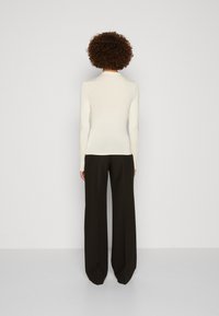 Långärmad, krämfärgad topp med en figurnära design, kombinerad med högmidjade, svarta vida byxor. Slät textur, minimal detaljering.