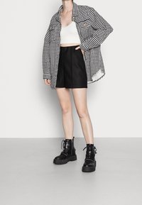 Černobílý houndstooth oversize kabát, bílý zkrácený top, černé šortky s vysokým pasem, černé šněrovací robustní boty, hladké textury látek.
