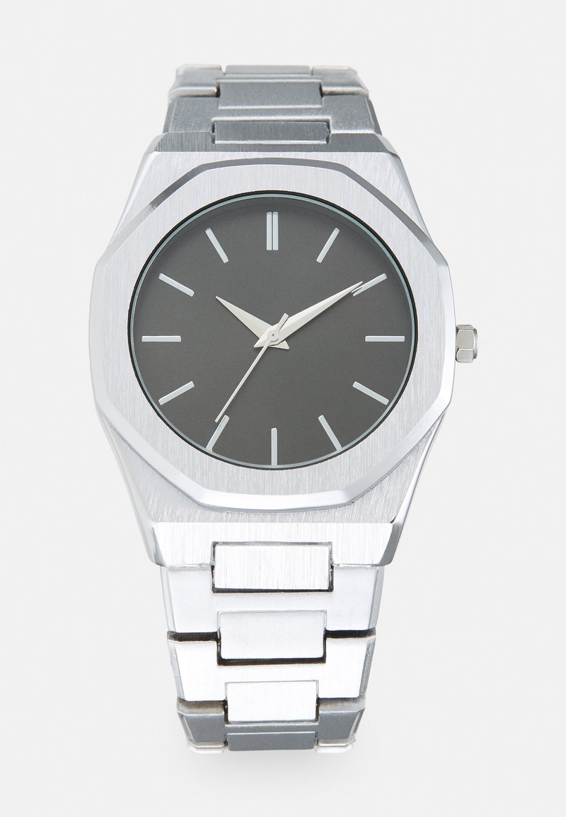 Sølv analog ur med et oktagonalt hus, grå urskive, sølvfarvede timeindikatorer og et armbånd af rustfrit stål. Minimalistisk design med en glat tekstur.