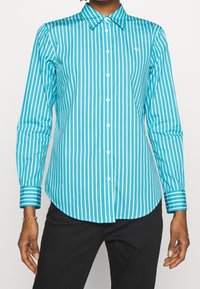 Turkos knapp-up skjorta med vertikala vita ränder, långa ärmar, en spetsig krage och en rundad nederkant med kontrasterande manschett-ränder.