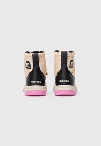 Ein Paar Sorel-Winterstiefel mit beigem gemustertem Stoff, schwarzen Lederelementen und leuchtend pinken Sohlen, von hinten gezeigt.