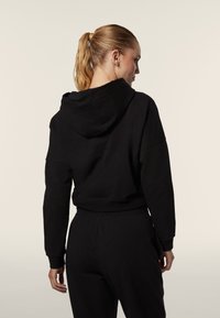 Haut à capuche noir coupé en coton mélangé, avec une poche kangourou et une capuche. Texture lisse, avec des poignets et un ourlet côtelés.