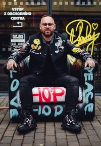 Black varsity jacket with colorful cartoon patches, ripped black jeans, and black sneakers with white accents, seated on a graffiti-decorated couch.
