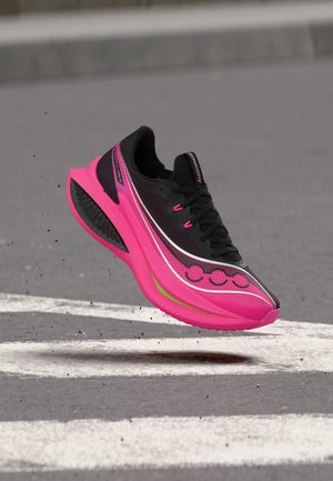 Schwarzer und knallig pinker Laufschuh in der Luft über einem Zebrastreifen, zeigt Seiten- und Bodendetails.