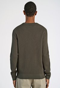 Olivinvihreä ribbineulepullover, jossa on pitkät hihat ja pyöreä kaula-aukko. Neuleessa on rakennepinta ja istuva helma, nähtynä takaa.